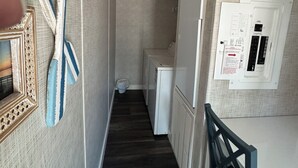 Kapea käytävä, jossa on puulattia, valkoinen jääkaappi ja seinälle asennettu sähkökeskus.