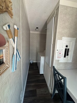 A narrow hallway with a wooden floor, a white refrigerator, and a wall-mounted electrical panel. - Happy Shores A Quaint 2-bedroom mobile home in Steinhatchee (Steinhatchee)