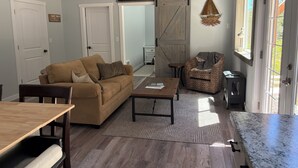 A spacious living area with a sofa, coffee table, and patterned armchair. A sliding barn door and a small table with a lamp are visible. - New 1-bedroom house in Garfield Bay perfect for a relaxing getaway (Sagle)