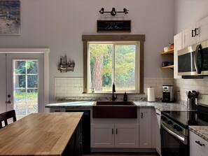 A kitchen with a large window, wooden cabinets, a stainless steel stove, and a microwave.