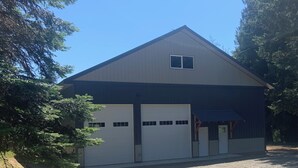 A single-story building with a gabled roof, two garage doors, and a small window. - New 1-bedroom house in Garfield Bay perfect for a relaxing getaway (Sagle)