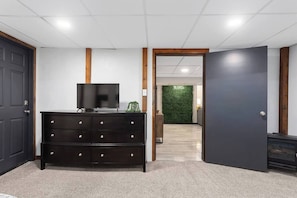 A hallway with a dark wooden dresser, a television on top, and a green wall with a sign. - Spacious King Beds! Quiet & Walkable | Fenced Yard (Lenexa)