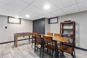 A room with a foosball table, a dining table with chairs, a bookshelf, and a door. - Spacious King Beds! Quiet & Walkable | Fenced Yard (Lenexa)