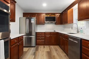 A modern kitchen with wooden cabinets, stainless steel appliances, and a built-in microwave. - Spacious King Beds! Quiet & Walkable | Fenced Yard (Lenexa)