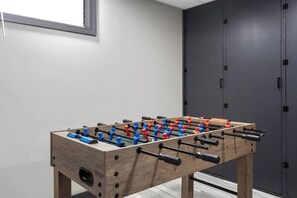 A wooden foosball table in a room with a grey wall and a dark door. - Spacious King Beds! Quiet & Walkable | Fenced Yard (Lenexa)