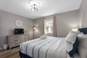 Ett sovrum med en säng, en tv på en byrå, en lampa och ett fönster med gardiner.