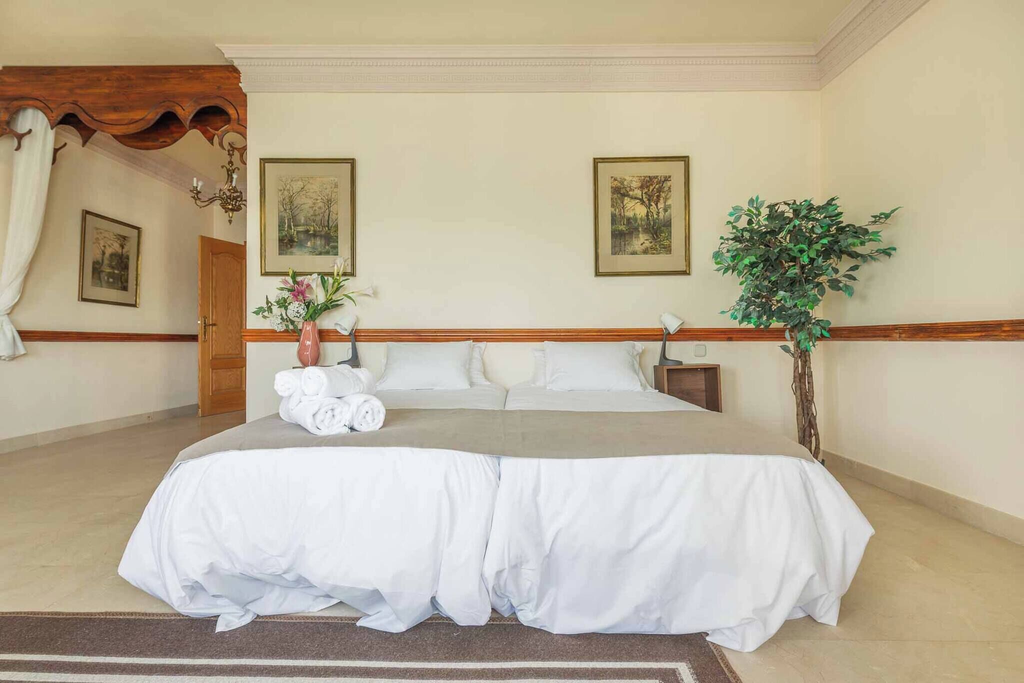 A neatly made bed with white linens, a wooden headboard, and a vase of flowers on the nightstand.