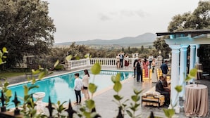 Ett poolområde med utsikt över bergen, en pergola och en sittgrupp med bord.