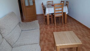 Quarto com sofá, uma pequena mesa de madeira, mesa de jantar com cadeiras e uma porta.