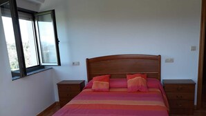 Uma cama de solteiro com cabeceira de madeira, duas mesas de cabeceira e uma janela com vista para árvores.