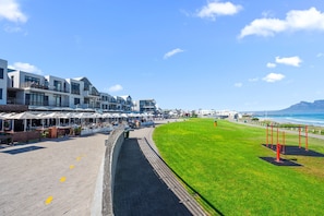 Un paseo marítimo costero con edificios modernos, una zona verde y vistas al océano.