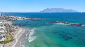 An aerial view of a coastal city with a prominent mountain, clear blue waters, and a beach. - Eden On The Bay 231 - Two Bedroom Apartment, Sleeps 4 (Cape Town)