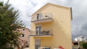 Un edificio a due piani con un balcone, un piccolo patio con posti a sedere all'aperto e un cortile lastricato.