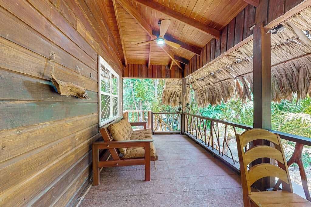 A wooden porch with a ceiling fan, a bench, and a chair.