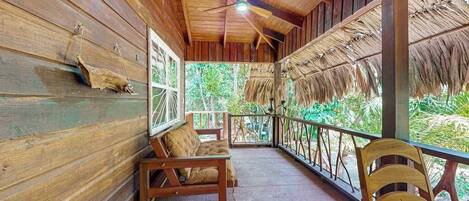 A wooden porch with a ceiling fan, a bench, and a chair.