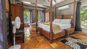 Uma cama de dossel em um quarto com um ventilador, janela e vista para o verde lá fora.