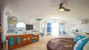 Une chambre à coucher avec un lit, une coiffeuse avec un miroir, un ventilateur de plafond et une vue sur la mer.