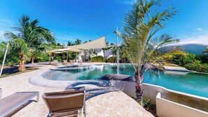 Un espace piscine avec des chaises longues, des palmiers et un ciel dégagé.