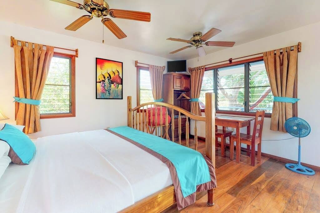 A bedroom with a bed, a desk, a chair, a fan, and a ceiling fan.