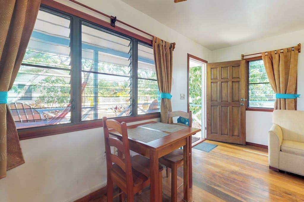 Una habitación con una mesa y sillas de madera, un sofá y ventanas grandes con cortinas.