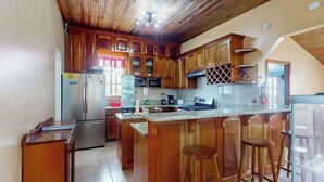 Une cuisine avec des meubles de rangement en bois, un réfrigérateur, un four à micro-ondes, une machine à café et un tabouret de bar.
