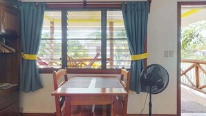 A room with a wooden table and chairs, a standing fan, and a window with curtains. - Romantic cabana w strong WiFi & shared pool, grill, enclosed yard-close to beach (Hopkins)
