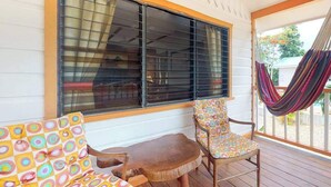 A covered outdoor seating area with a wooden table and two chairs, a large window with blinds, and a hammock. - Romantic cabana w strong WiFi & shared pool, grill, enclosed yard-close to beach (Hopkins)