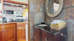 A bathroom with a stone wall, a round mirror, a sink, and a towel basket. - Romantic cabana w strong WiFi & shared pool, grill, enclosed yard-close to beach (Hopkins)