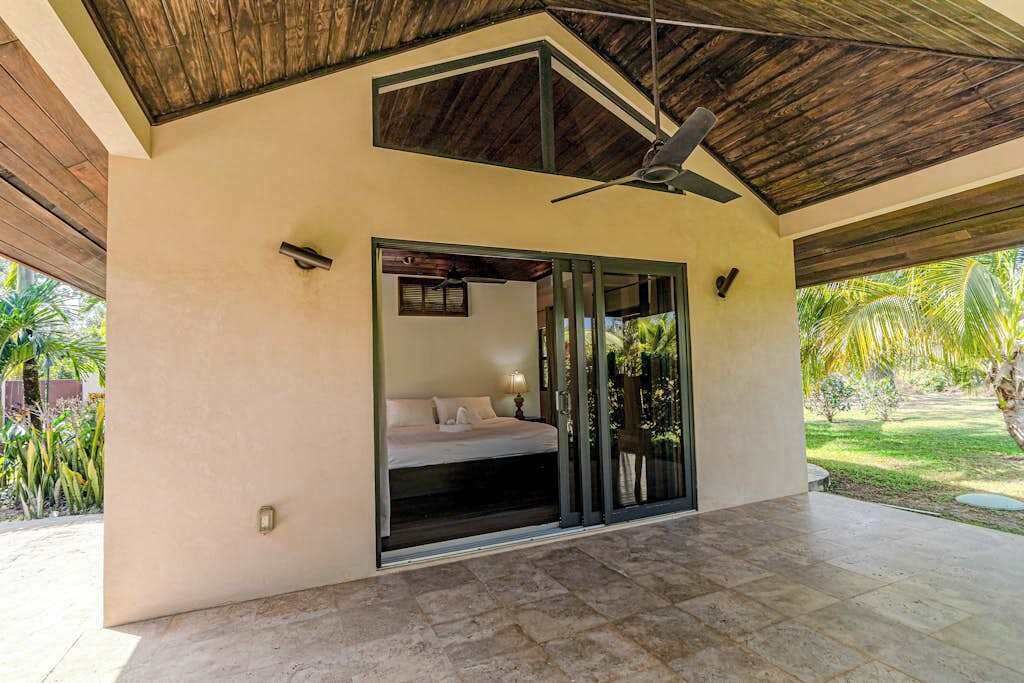 Une chambre moderne avec un lit, un ventilateur de plafond et une porte-fenêtre coulissante donnant sur un jardin.