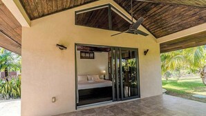 Un dormitorio moderno con cama, ventilador de techo y puerta corrediza de vidrio que da a un jardín.