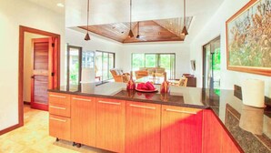 Una cocina moderna con una isla grande, armarios de madera, iluminación colgante y vistas al exterior.