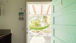 Una puerta que da a un espacio exterior con una hamaca, una casa al fondo y una puerta verde.