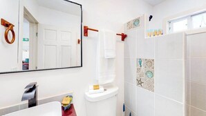Un baño con inodoro blanco, espejo, toallero y zona de ducha con azulejos decorativos.