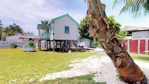 A white building with a green roof, a palm tree, and a bicycle. - Colorful studio cabana with WiFi, partial AC, yard & picnic area - walk to town (Caye Caulker)