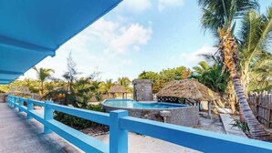 Un área de piscina con barandilla azul, palmeras y estructuras de techo de paja.