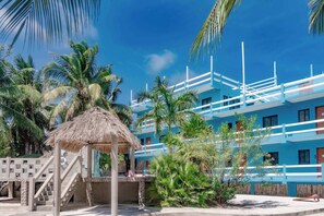 A resort with a thatched-roof structure, palm trees, and a blue building with balconies. - Cozy Suite w/ WiFi, AC, Shared Sundeck, & Pool - Rooftop with Great Views (Caye Caulker)