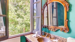 Un baño con un espejo grande, un lavamanos y una ventana con vistas a la vegetación.