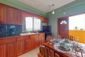 A kitchen with wooden cabinets, a dining table set with plates and glasses, and a window with a view. - Charming apartment with ocean views from the rooftop, free WiFi & partial AC (San Pedro)