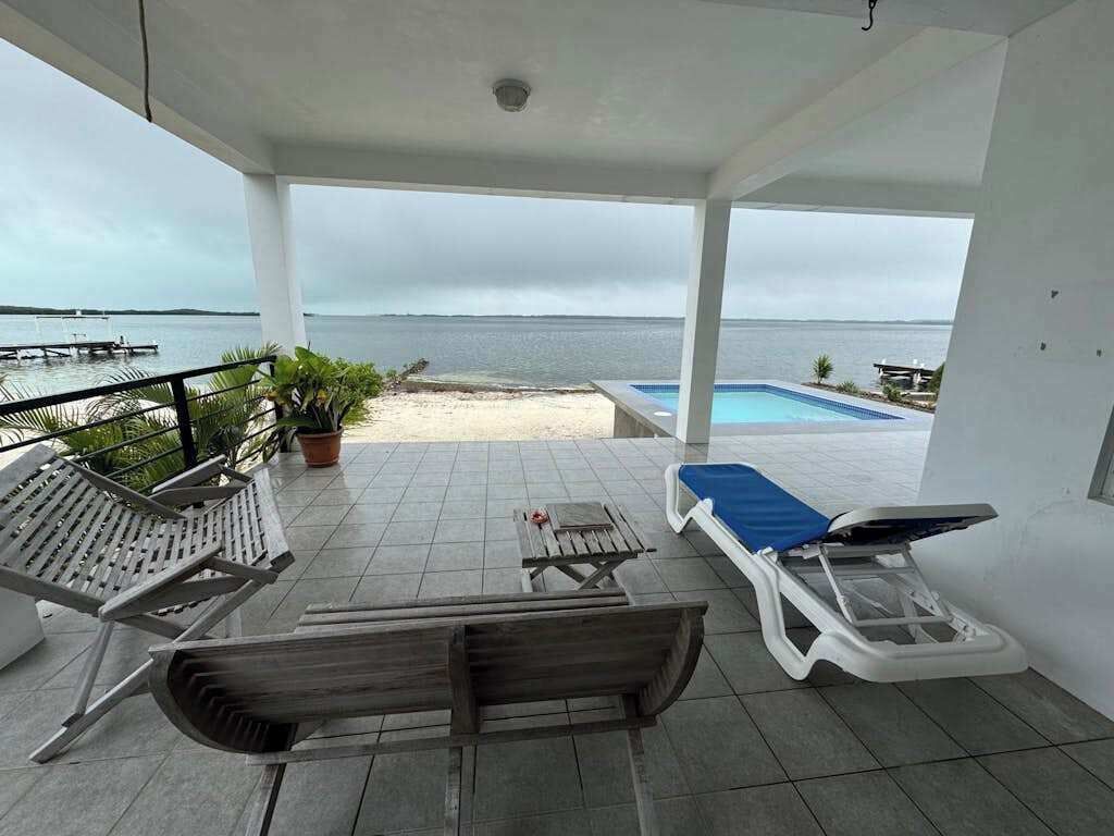 A covered outdoor area with lounge chairs, a pool, and a view of the sea.