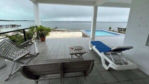 A covered outdoor area with lounge chairs, a pool, and a view of the sea. - Waterfront home in a quiet area with amazing views, pool, lanai & hammock (San Pedro)