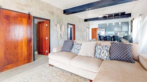 A living room with a sofa, wooden doors, a kitchen in the background, and a ceiling fan. - Waterfront home in a quiet area with amazing views, pool, lanai & hammock (San Pedro)