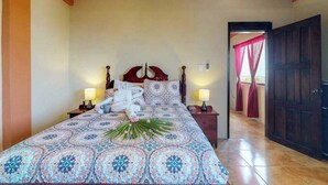 A bedroom with a patterned bedspread, a wooden headboard, two bedside lamps, and a nightstand with a lamp. - Inviting apartment w WiFi & partial AC - steps from the ocean, walk everywhere (San Pedro)