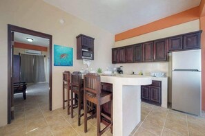 A kitchen with dark wooden cabinets, a white island with bar stools, a microwave, and a refrigerator. - Charming apartment w amazing rooftop view, WiFi & partial AC - walk everywhere (San Pedro)
