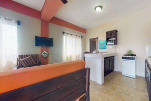 A living room with a sofa, a television, a kitchen with a stove, and a microwave. - Charming apartment w amazing rooftop view, WiFi & partial AC - walk everywhere (San Pedro)