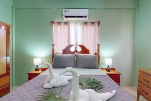 Een slaapkamer met een bed, twee nachtkastjes met lampen, een houten garderobe en een airconditioner.