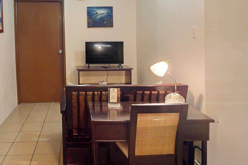 A dining area with a wooden table, chairs, a television, and a lamp.