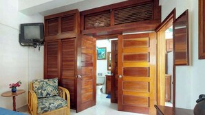 Una habitación con una cama, una silla, puertas de madera, un televisor y vistas a otra habitación.