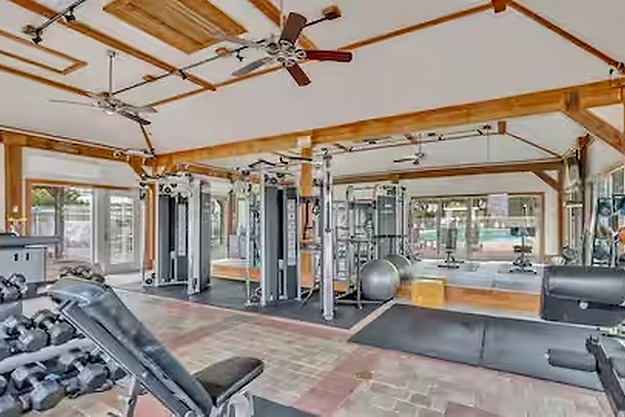 A gym with ceiling fans, exercise equipment, and large windows.