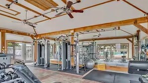 A gym with ceiling fans, exercise equipment, and large windows.