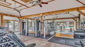 A gym with ceiling fans, exercise equipment, and large windows.